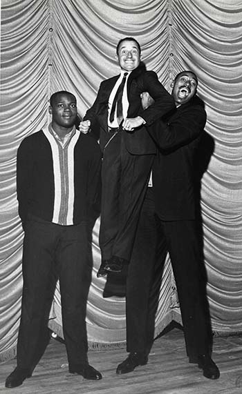Basketball player Wilt “the Stilt” Chamberlain hoists John Ascuaga up to his height while his team member Howie Montgomery watches (