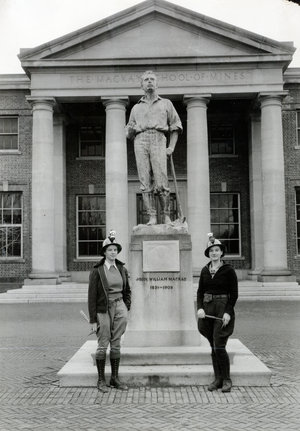 Two young women mining students in hardhats pose next Mackay statue, antique photo