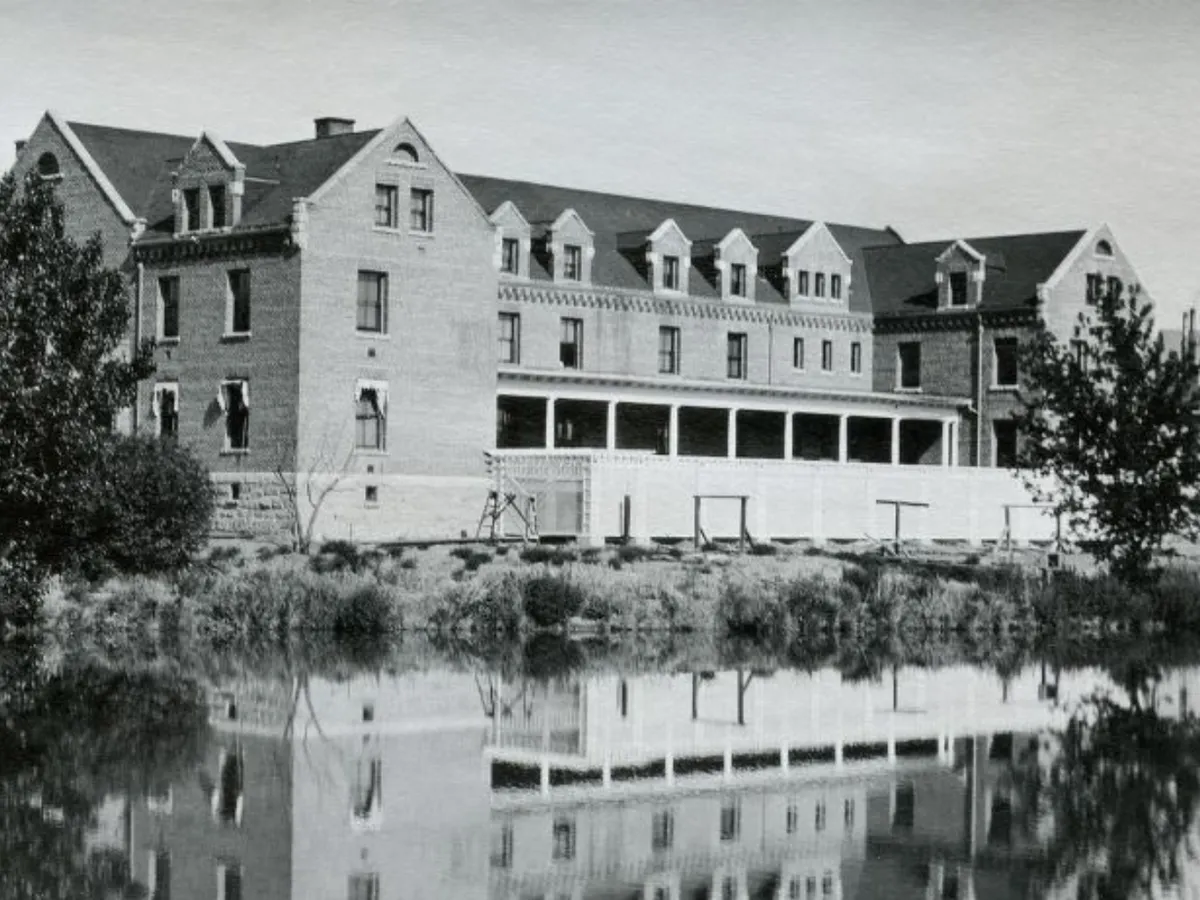 1911 black and white photo of Manzanita Hall with small trees next to the building and the building's reflection visible in Manzanita Lake.