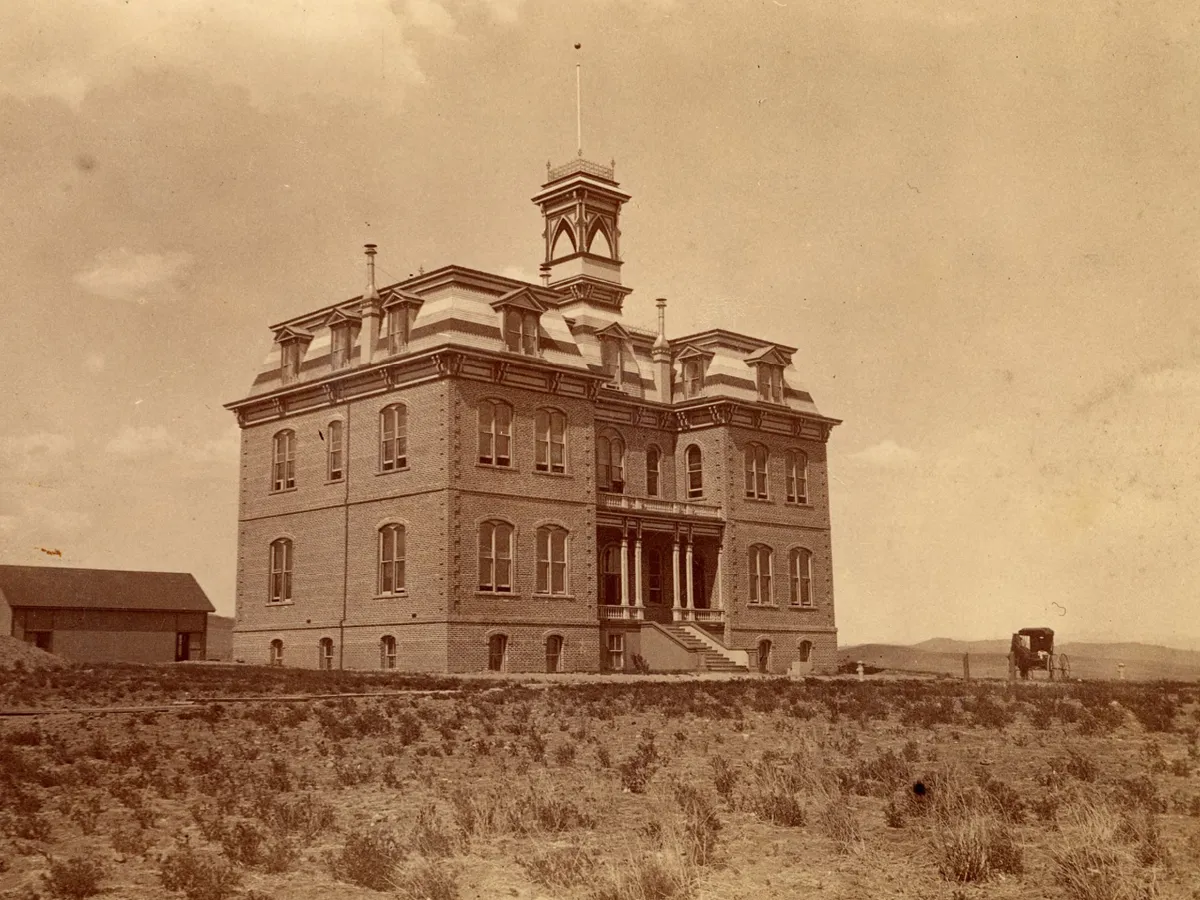 Morrill Hall is seen here at a distance shortly after construction was finished with the caption on the image reading, "State University. Reno, Nevada" (photographic print, 4.5 x 8 inches). A small, wooden building is seen in the left of the photo and a horse and buggy carriage is seen to the right.