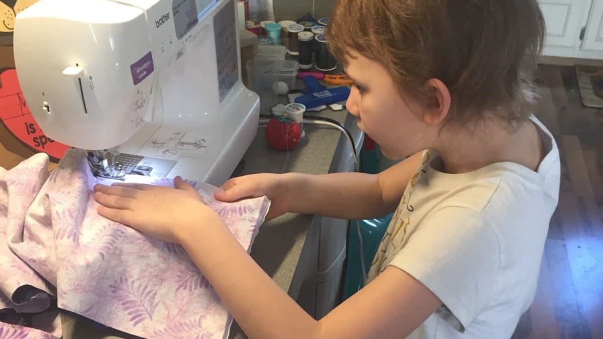 Young girl using a sewing machine to sew pink palm leaf printed cloth
