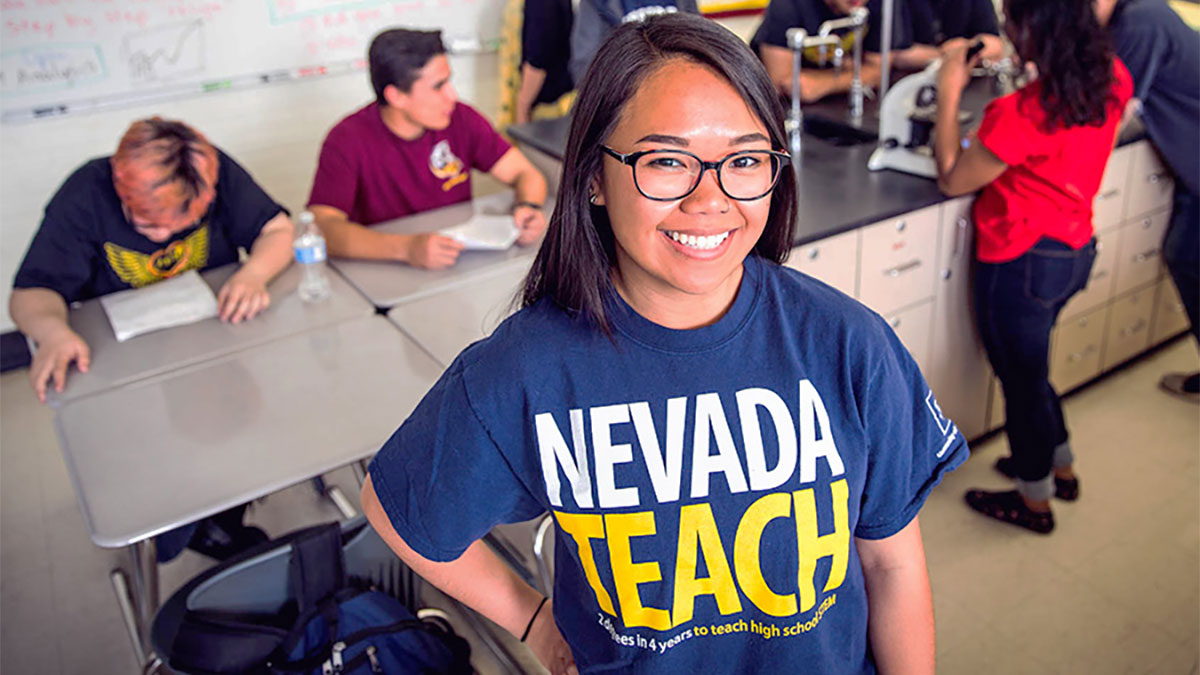 NevadaTeach student smiling with students in the background working on science project