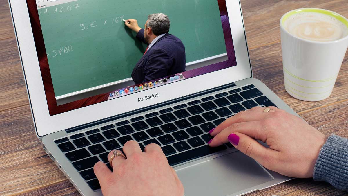 laptop showing man writing on green chalkboard