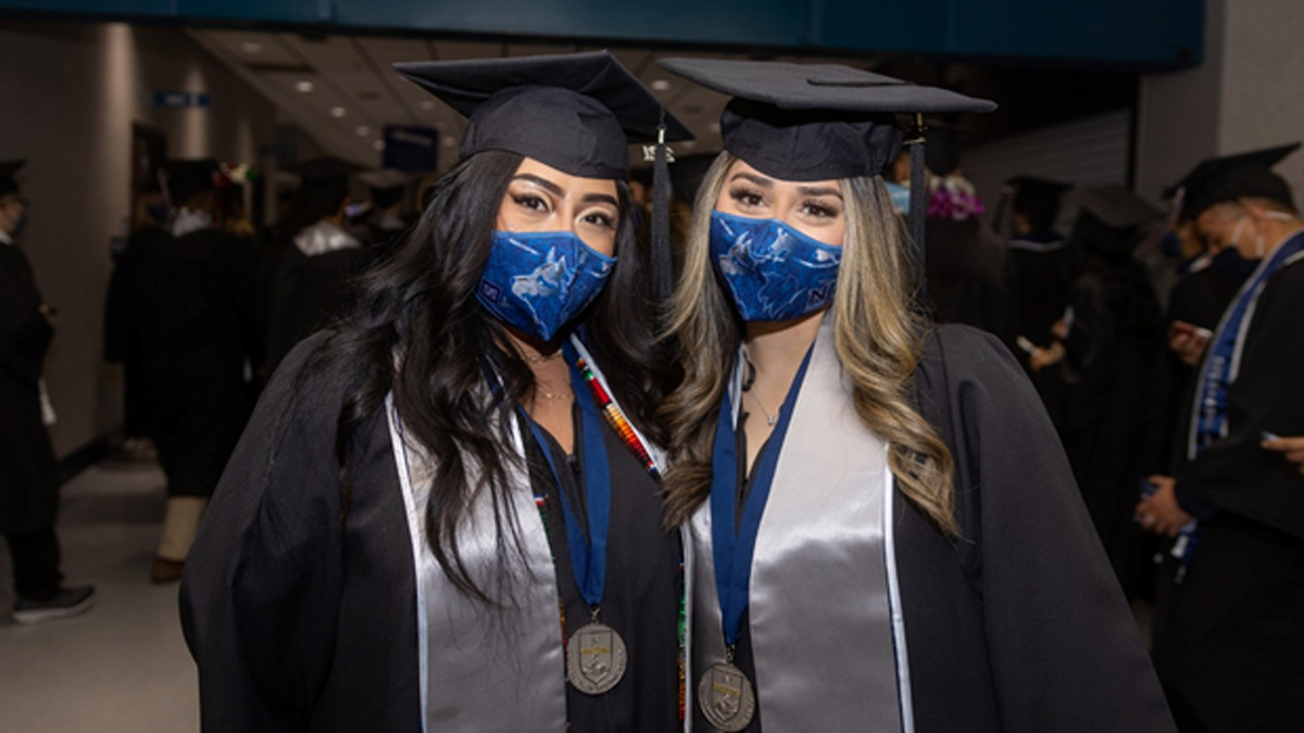 In Lawlor, two graduates pose for a photo in their caps, gowns, medals, sashes and matching Wolf Pack masks.
