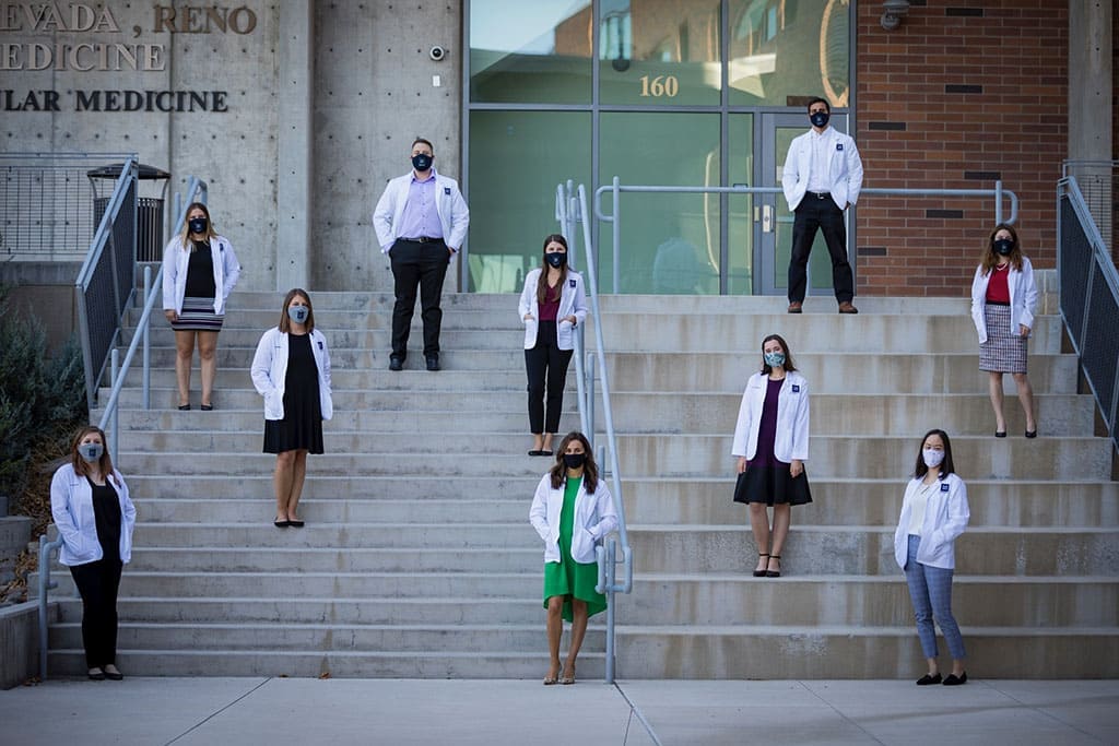 Group of 10 med students standing socially distanced wearing white coats and masks