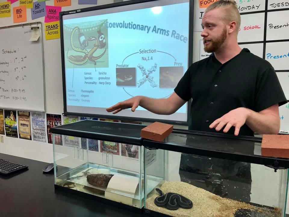 Student giving a lecture motioning to two terrariums with snakes. 