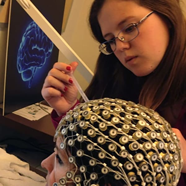 A researcher touches the monitoring equipment that is placed on a subject's head.
