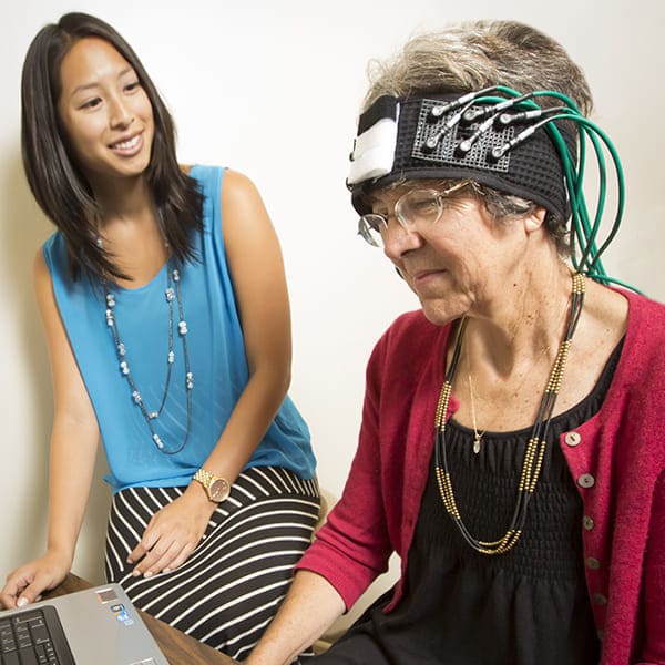 A researcher monitors a person who is wearing a monitoring equipment on their head.