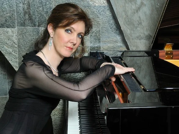 Anne-Marie McDermott rests her arms on a piano as she sits for a publicity photo.