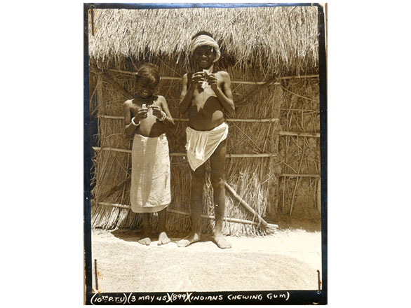 Old photograph from World War II era in Bengal, India of two children smiling outside straw hut