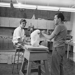 Joan Arrizabalaga is seated next to student sculptor Ron Moroni who is working on a piece in a studio (circa 1960). Photo credit: University Archives, University of Nevada, Reno.
