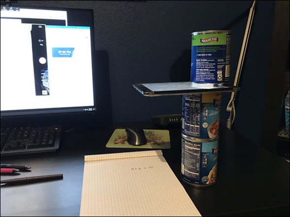 Desk showing a makeshift document camera consisting of 3 soup cans and an iPad. The soup cans are stacked and the iPad is placed between the top two cans with the camera aligned over a notepad.