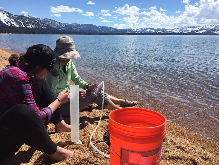 Two scientists hold a tube for microplastic sampling with Lake Tahoe and mountains in the background.