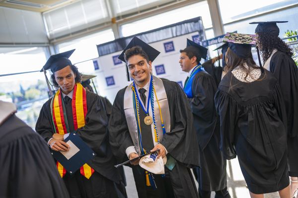 Graduates show off decorated caps outside the Latinx Graduate Celebration, with the cap in the foreground reading "Mi familia, los que hacen que todo valga la pena"