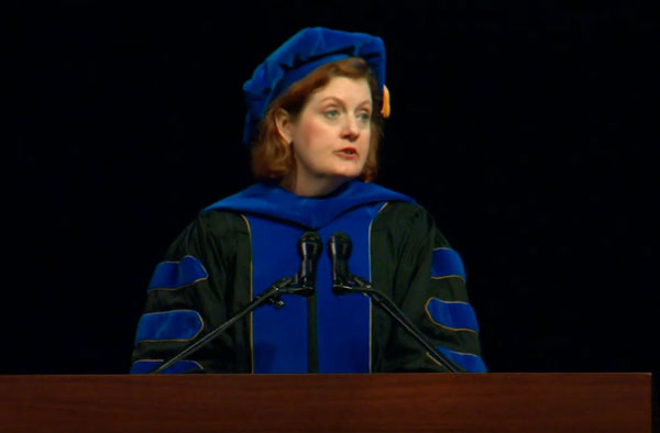 Woman speaking at a lectern wearing graduation attire.
