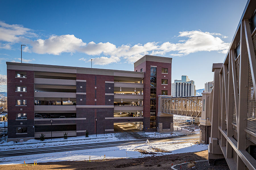 Seven story brick parking complex connected to a beige bridge, surrounded by a blue sky and white snow on the ground.