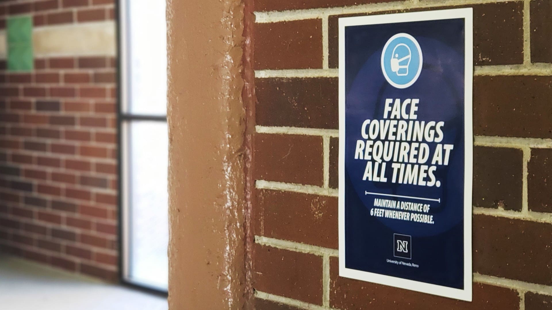 A poster indicating that face coverings are required at all times on the wall of a parking garage