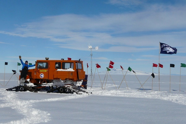 Researcher with a snow cat vehicle and a Wolf Pack flag in Antarctica