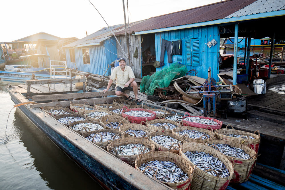 Zeb Hogan standing next to a fishing boat full of baskets of caught fish