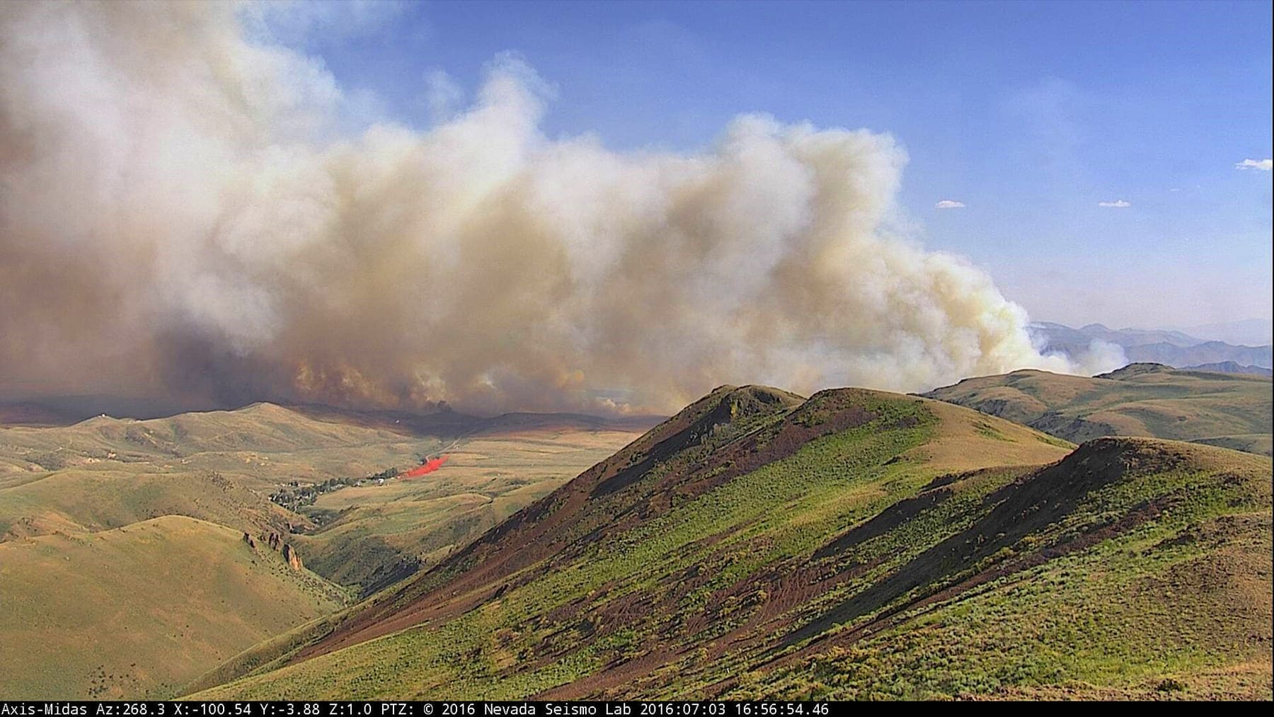 A wildfire's smoke column billowing up from a hill captured by the AlertWildfire camera system