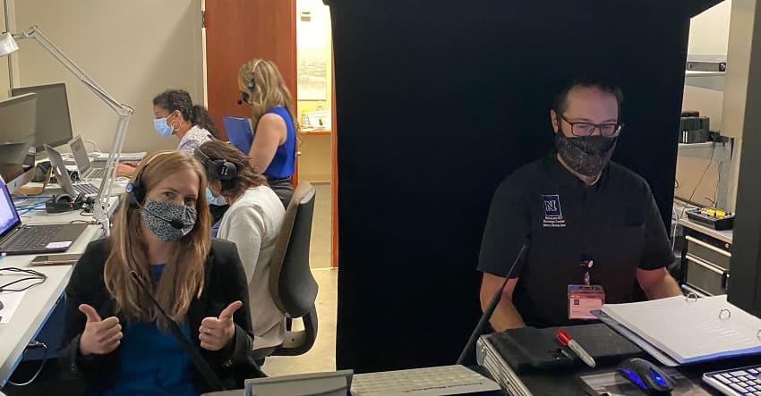 Michelle Rebaleati (left) giving a thumbs up before the Virtual Homecoming Alumni Awards Event while Kyle Weerheim (right) gets prepped to video switch the show. Jeanne Corbit’s University Events team preps for the show in the background.