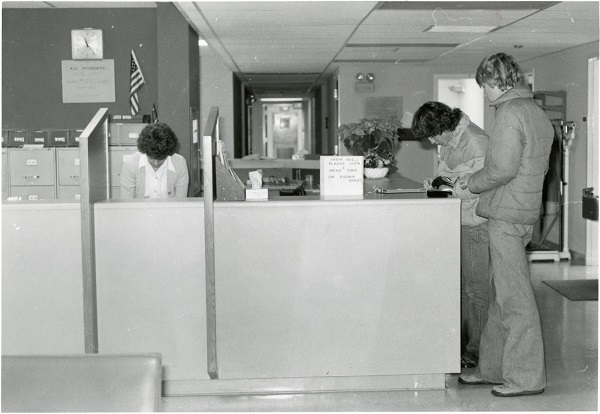 Students wearing bell-bottoms signing in at the old Student Health Center on the ground floor of Juniper Hall in the 1970s