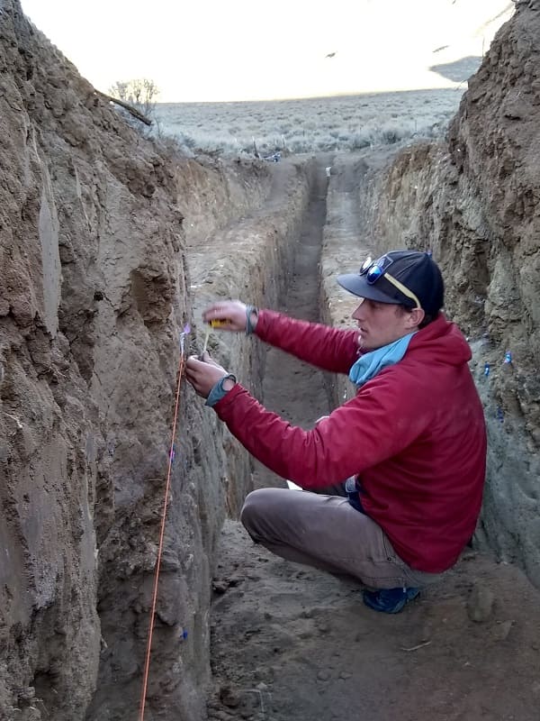A geologist crouched in the cleared out Ridgecrest fault taking measurements