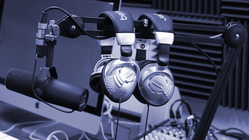 Grey gradient image of headphones and microphones in a podcast recording studio.