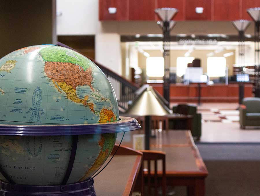 A close-up of a globe, with the library tables and circulation desk in the background