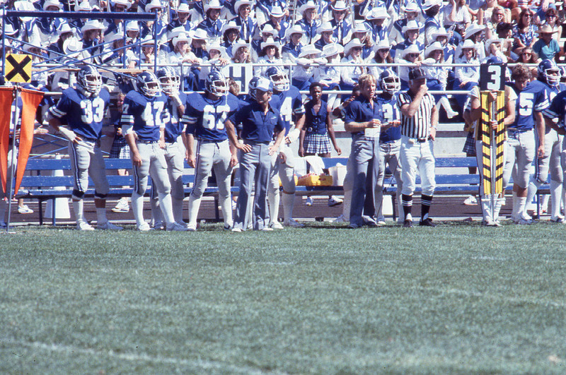 Chris Ault on the field with Wolf Pack football players and a crowd behind them