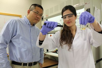 Female graduate student in lab coat shows substance in test tubes to male researcher