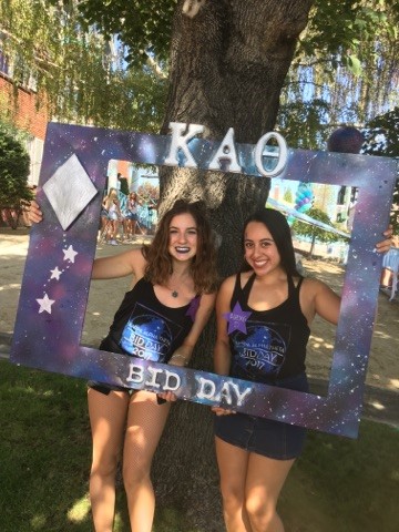 Two Kappa Alpha Theta Sisters stand on a house lawn during Bid Day