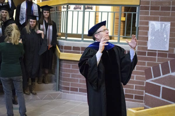 The dean speaks in front of the graduating class of students in the atrium.