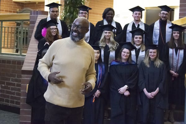 Faculty speaks to group with students in regalia in the background.