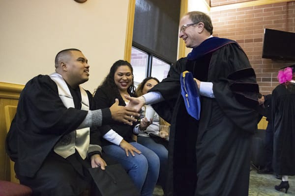 The dean shakes a students hand while his parents sit next to him.
