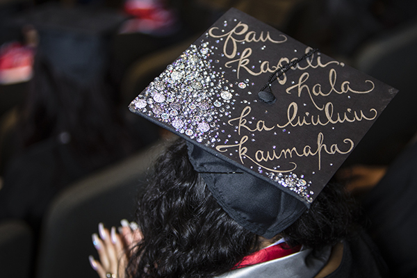 A graduate's cap reads "Pau kapali hala ka lu'ulu'u kaumaha" at the Asian American & Pacific Islander Graduate Celebration