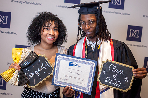 Smiling graduates holding a certificate and chalk boards at the American Indian & Alaskan Native Graduate Celebration