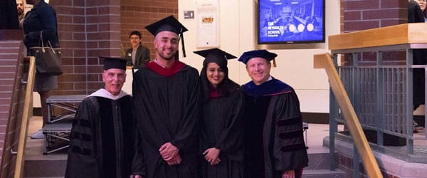 Students and faculty pose in regalia indoors.