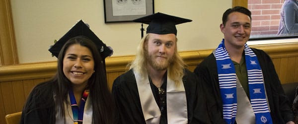 Three students post indoors in regalia.