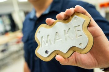 A plaque made on the lasercutter in the makerspace; it has the word "make" on it.