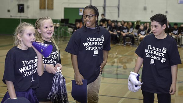 Four middle school students at Clayton Middle School wear "Future Wolf Pack Student" T-shirts while leading fellow students in a cheer