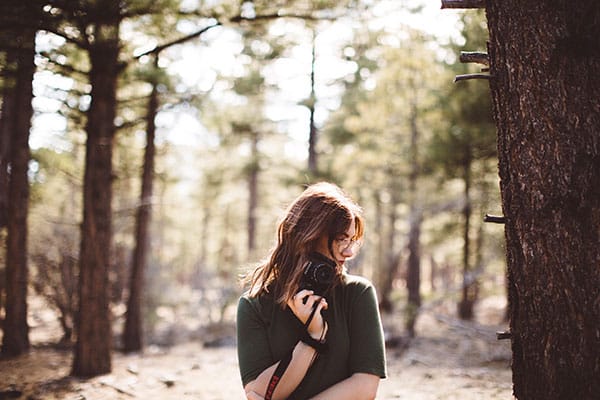 Student poses in the woods, holding a camera.