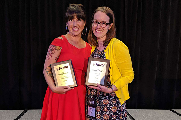 Two women pose on stage holding plaques.