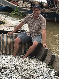 Zeb Hogan sits in boat with fish in Cambodia