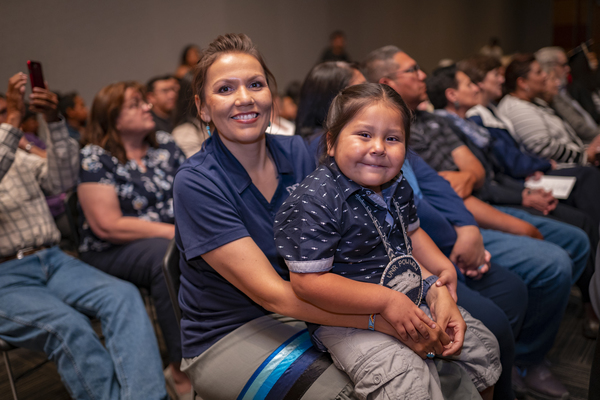 A smiling child sits on the lap of a student speaker at the American Indian & Alaskan Native Graduate Celebration