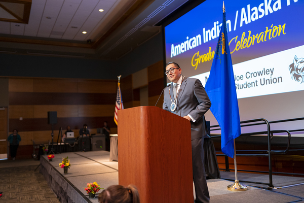 A speaker at the podium addressing the audience at the American Indian & Alaskan Native Graduate Celebration