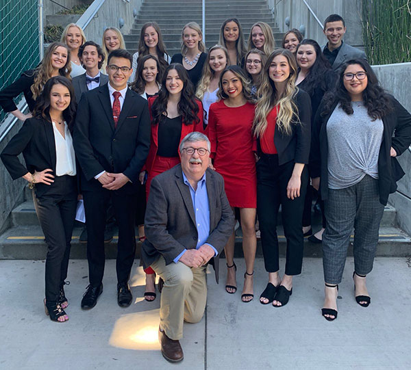 More than 20 students and a faculty member pose on stairs outdoors.