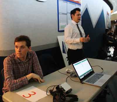 Two students talk to the public about their capstone project, with a computer and light prototype on a table
