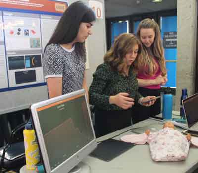 Two students talk to the public about their capstone project, with a computer and light prototype on a table