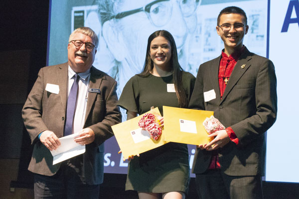 Faculty member and students pose on stage, holding awards.